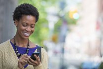 Mujer adulta mediana con teléfono inteligente de comprobación de pelo corto y sonriendo en la calle . - foto de stock