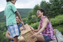 Familia con niño de edad elemental sosteniendo cesta de picnic en el muelle . - foto de stock