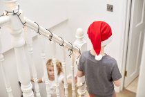 Età elementare ragazzo a Babbo Natale cappello e ragazza correre giù per le scale . — Foto stock