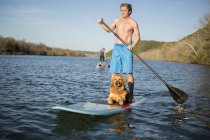 Man standing on paddleboard with dog on lake water. — Stock Photo