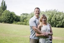 Couple standing in park, smiling and embracing. — Stock Photo