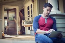 Man using digital tablet on porch on countryside house. — Stock Photo