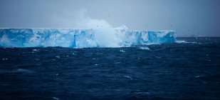 Large steep iceberg floating on spraying water with waves. — Stock Photo