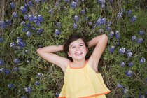 Elementary age girl lying on grass amid wild flowers, overhead view. — Stock Photo