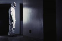 Man in hazardous material protective suit facing bright light in hallway. — Stock Photo