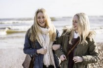 Due giovani donne a braccetto sulla spiaggia in inverno . — Foto stock