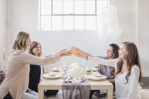 Quatro mulheres sentadas na mesa baixa e levantando copos em torradas . — Fotografia de Stock