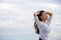 Long-haired woman enjoying breeze outdoors against cloudy sky. — Stock Photo