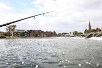 Fishing rod against water by weir and bridge of town in England. — Stock Photo
