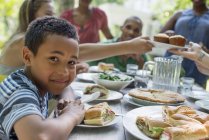 Boy smiling at table with family gathering around dinner table in countryside garden. — Stock Photo