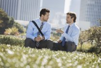 Двое мужчин в футболках и галстуках сидят и разговаривают в городском парке . — стоковое фото