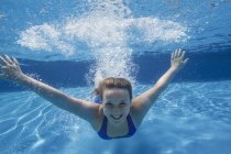 Cheerful pre-adolescent girl swimming underwater in pool. — Stock Photo