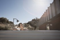 Человек принимает душ на открытом воздухе на террасе дома под солнечным светом . — стоковое фото