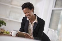 Woman in black jacket using digital tablet and holding cup in office. — Stock Photo