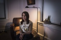 Женщина средних лет сидит с грустным выражением лица на диване в темной комнате . — стоковое фото