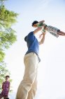 Low angle view of father playing and lifting elementary age boy outdoors. — Stock Photo