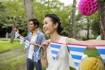 Young couple hanging lanterns and flags on trees in woods. — Stock Photo