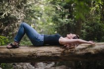 Woman lying on back on fallen tree trunk in woodland. — Stock Photo