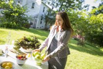Жінка в саду ферми готує стіл зі свіжими органічними овочами та фруктами . — стокове фото
