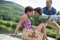 Father carrying son on pier with mother and picnic basket at lake. — Stock Photo