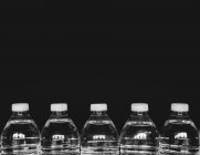 Fila de botellas de agua de plástico transparente llenas de agua filtrada sobre fondo negro . - foto de stock