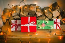 Gift boxes tied with ribbons and fairy lights on logs, still life. — Stock Photo