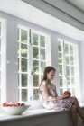 Menina idade elementar sentado no peitoril da janela com tigela de frutas . — Fotografia de Stock