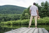 Вид сзади на человека, стоящего на деревянном пирсе с видом на спокойное озеро . — стоковое фото