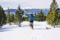 Vue arrière de l'homme courant à travers la neige profonde à flanc de montagne . — Photo de stock
