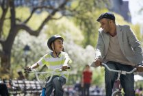 Père et fils faisant du vélo côte à côte dans un parc ensoleillé . — Photo de stock