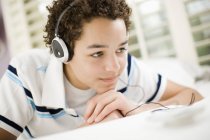 Pre-adolescent boy with headphones lying on front of bed. — Stock Photo
