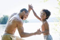 Father wrestling elementary age boy by lake. — Stock Photo