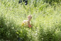 Femme parmi les fleurs et l'herbe verte haute à la pépinière . — Photo de stock