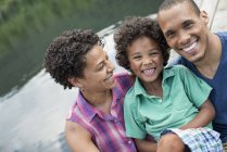 Portrait of happy parents and elementary age boy by lake in summer. — Stock Photo