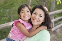 Mutter posiert im Park mit Tochter, lächelt und blickt in die Kamera. — Stockfoto