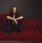 Donna in nero abbigliamento casual seduta sul divano rosso
. — Foto stock