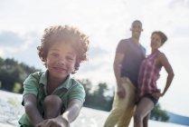 Хлопчик елементарних віку сидять на Сонячний озеро jetty з батьками. — стокове фото
