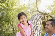 Elementary age girl sitting on tree trunk beside father and looking in camera. — Stock Photo