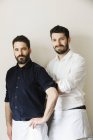 Half-length portrait of two bearded men in white aprons looking in camera. — Stock Photo
