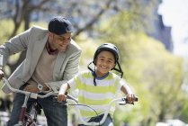 Pai e filho de bicicleta lado a lado em um parque ensolarado . — Fotografia de Stock