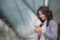 Jovem empresária de jaqueta cinza sorrindo e usando smartphone . — Fotografia de Stock