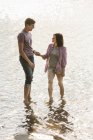 Couple holding hands while paddling in shallow water at lake. — Stock Photo