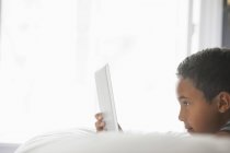 Vista lateral do menino idade elementar usando tablet computador na cama . — Fotografia de Stock