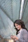 Joven empresaria en cárdigan gris usando smartphone y sonriendo en la ciudad . - foto de stock
