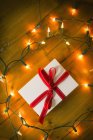 Caja de regalo atada con cinta roja y luces de hadas en suelo de madera . - foto de stock