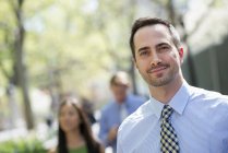 Mid adult man smiling and looking in camera with couple in background. — Stock Photo