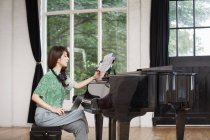 Young woman sitting at grand piano in rehearsal studio and annotating sheet music. — Stock Photo