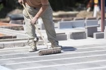 Cropped view of man using brush on cement floor on construction site. — Stock Photo