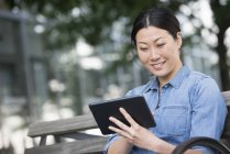 Mid adult woman sitting on bench and using digital tablet. — Stock Photo