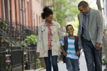 Dois pais e menino de idade elementar andando juntos na rua da cidade . — Fotografia de Stock